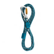 The Rope Dog Leash Thin Deep Teal is coiled in a figure-eight shape, secured with two blue clips, and attached to a silver carabiner featuring a gold locking mechanism.