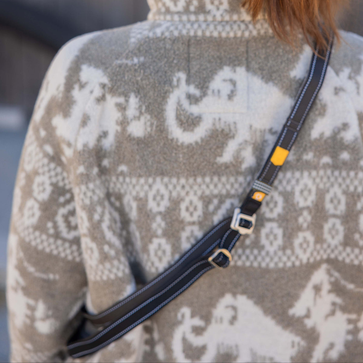 Person from behind wearing a grey and white patterned fleece jacket and a crossbody bag.
